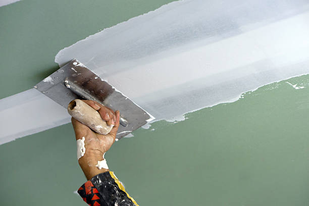 Professional applying drywall joint compound and repairing a wall seam for seamless texture matching by a house painter in Little Elm.